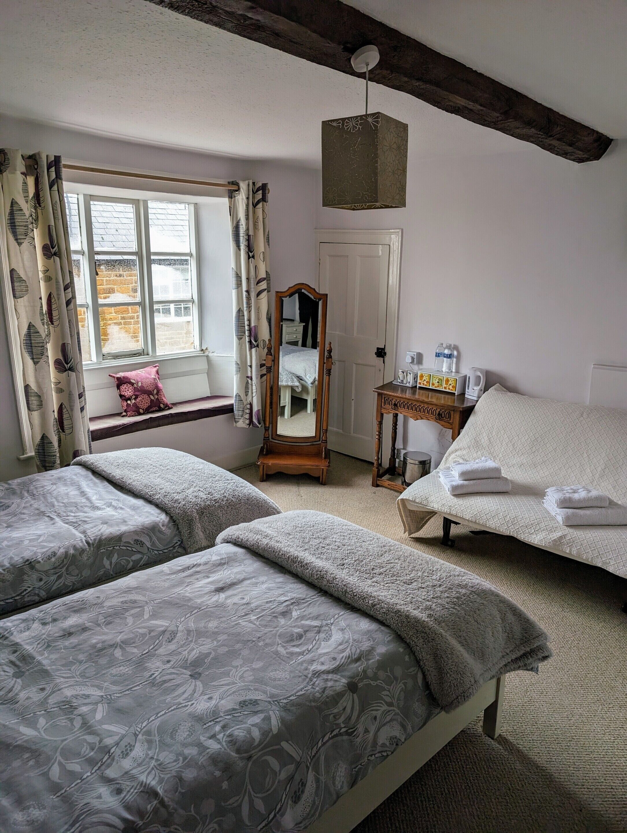 A bedroom with two beds, a mirror, a dresser, and a window with curtains.
