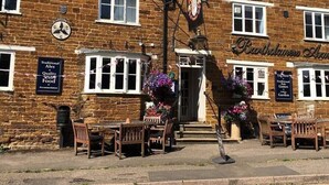 A traditional brick building with a sign reading "Bartholomew Arms" and "Traditional Ales & Quality Food." There are outdoor seating areas with tables and chairs. - Bartholomew Arms (Towcester)