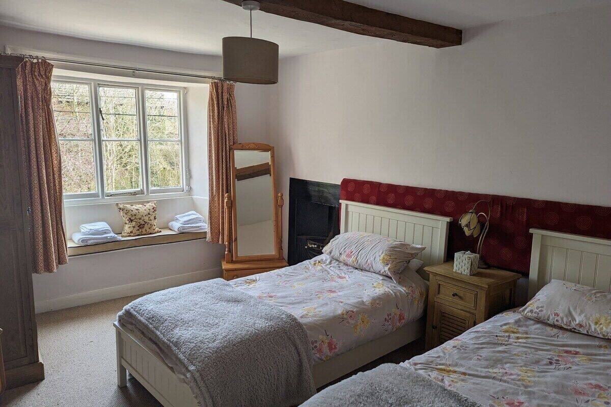A bedroom with two beds, a window with curtains, a mirror, and a bedside table with a lamp.