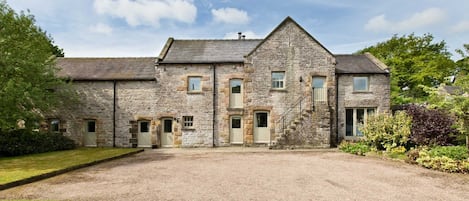 A stone building with multiple windows and doors, a gravel driveway, and surrounding greenery.