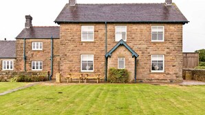 A stone house with a gabled front, multiple windows, and a small garden with a bench. - Stylish Farmhouse with stunning views over rolling hills and fabulous games room. (Belper)