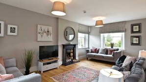 A living room with a fireplace, sofa, TV, and artwork on the walls. - Stylish Farmhouse with stunning views over rolling hills and fabulous games room. (Belper)