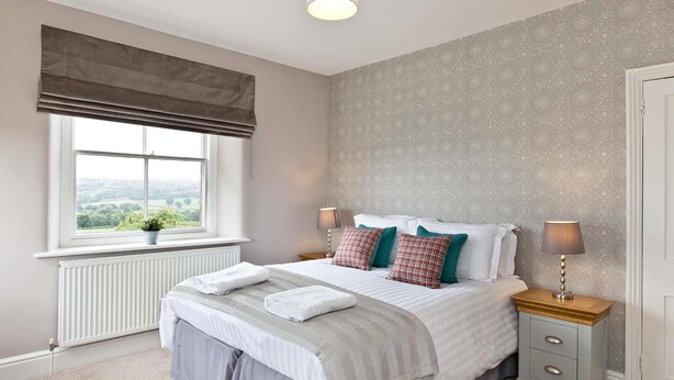 A bedroom with a large window, a bed with white bedding, two bedside lamps, and a radiator. - Stylish Farmhouse with stunning views over rolling hills and fabulous games room. (Belper)