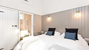 A bedroom with a large bed, two bedside tables, a nightstand, a wall-mounted light fixture, and a door leading to a bathroom. - Collection of 4 charming barns offering group accommodation for 16, close to Bakewell (Bakewell)