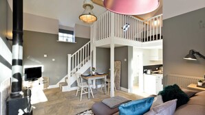 A spacious living area with a high ceiling, a staircase leading to an upper level, a dining area, and a kitchen. - Collection of 4 charming barns offering group accommodation for 16, close to Bakewell (Bakewell)
