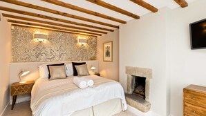 Un dormitorio con una cama, dos lámparas de noche, una chimenea y un televisor montado en la pared.