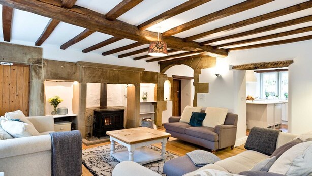 A cozy living room with exposed wooden beams, a fireplace, and a comfortable seating area. - Traditional 5 bedroom stone built farmhouse, near Monsal Trail and Bakewell. (Bakewell)