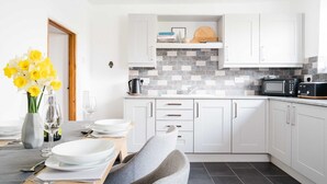 Uma cozinha moderna com armários brancos, painel de azulejos e um espaço de refeições com mesa posta para dois.