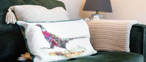 A green sofa with a white pillow featuring a colorful bird design and a beige knitted throw.