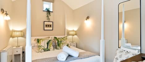 A bedroom with a four-poster bed, bedside lamps, a small window, and a mirror.