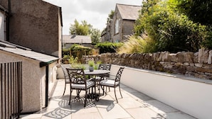A patio with a round table and chairs, a stone wall, and a stone building in the background. - Cosy 2 bed cottage nestled in the village of Bradwell, close to the Hope Valley (Bradwell)
