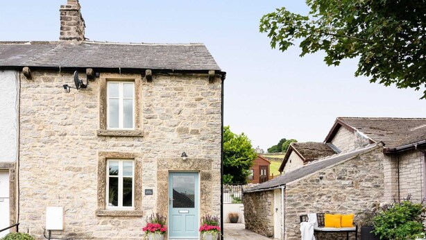 A stone cottage with a light blue door, a small garden with pink flowers, and a visible sign indicating it is a guesthouse. - Cosy 2 bed cottage nestled in the village of Bradwell, close to the Hope Valley (Bradwell)