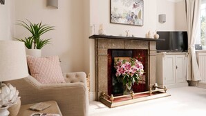 A living room with a fireplace, a sofa, a television, and a potted plant. - Quaint 2 bedroom cottage in the picturesque village of Ashford-in-the-Water. (Bakewell)