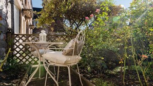A garden patio with a metal table and chairs, surrounded by a wooden lattice fence and lush greenery. - Quaint 2 bedroom cottage in the picturesque village of Ashford-in-the-Water. (Bakewell)