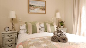 A neatly arranged bedroom with a bed, two bedside tables, a nightstand, a clock, and a painting on the wall. - Quaint 2 bedroom cottage in the picturesque village of Ashford-in-the-Water. (Bakewell)
