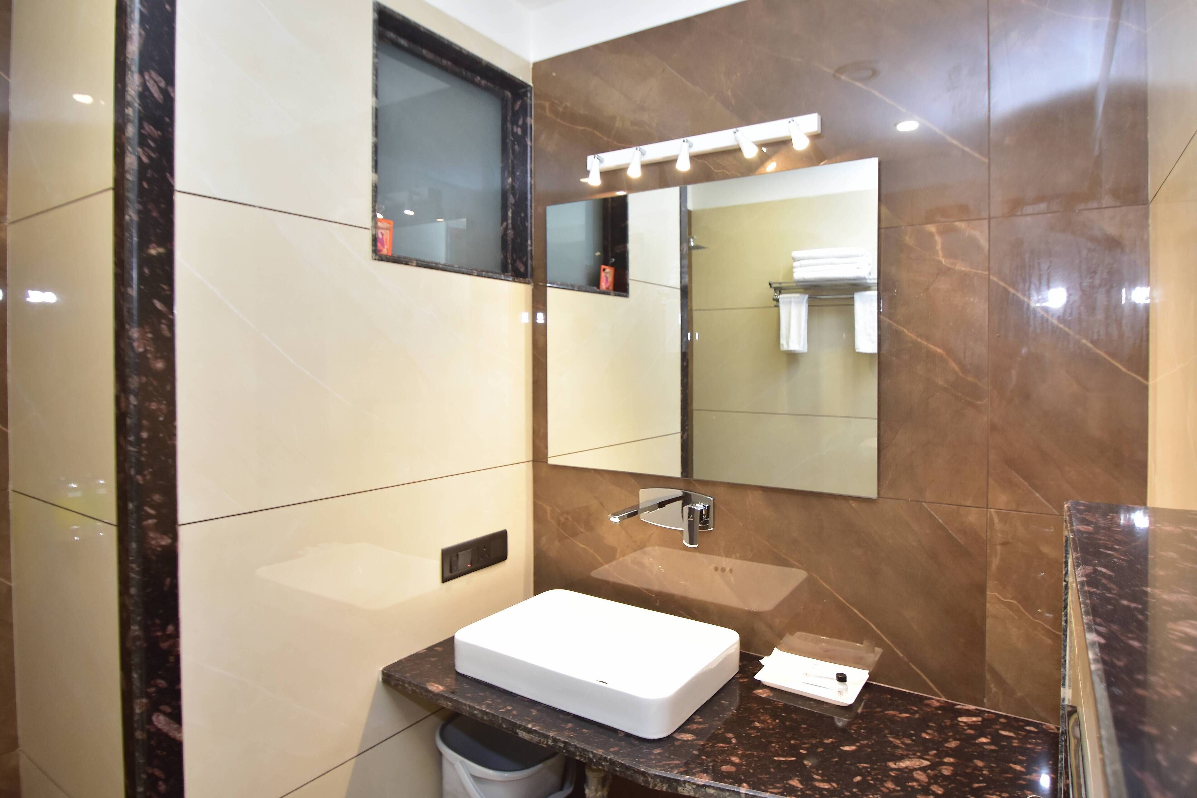 A modern bathroom with a white sink, a large mirror, and a marble-tiled wall.