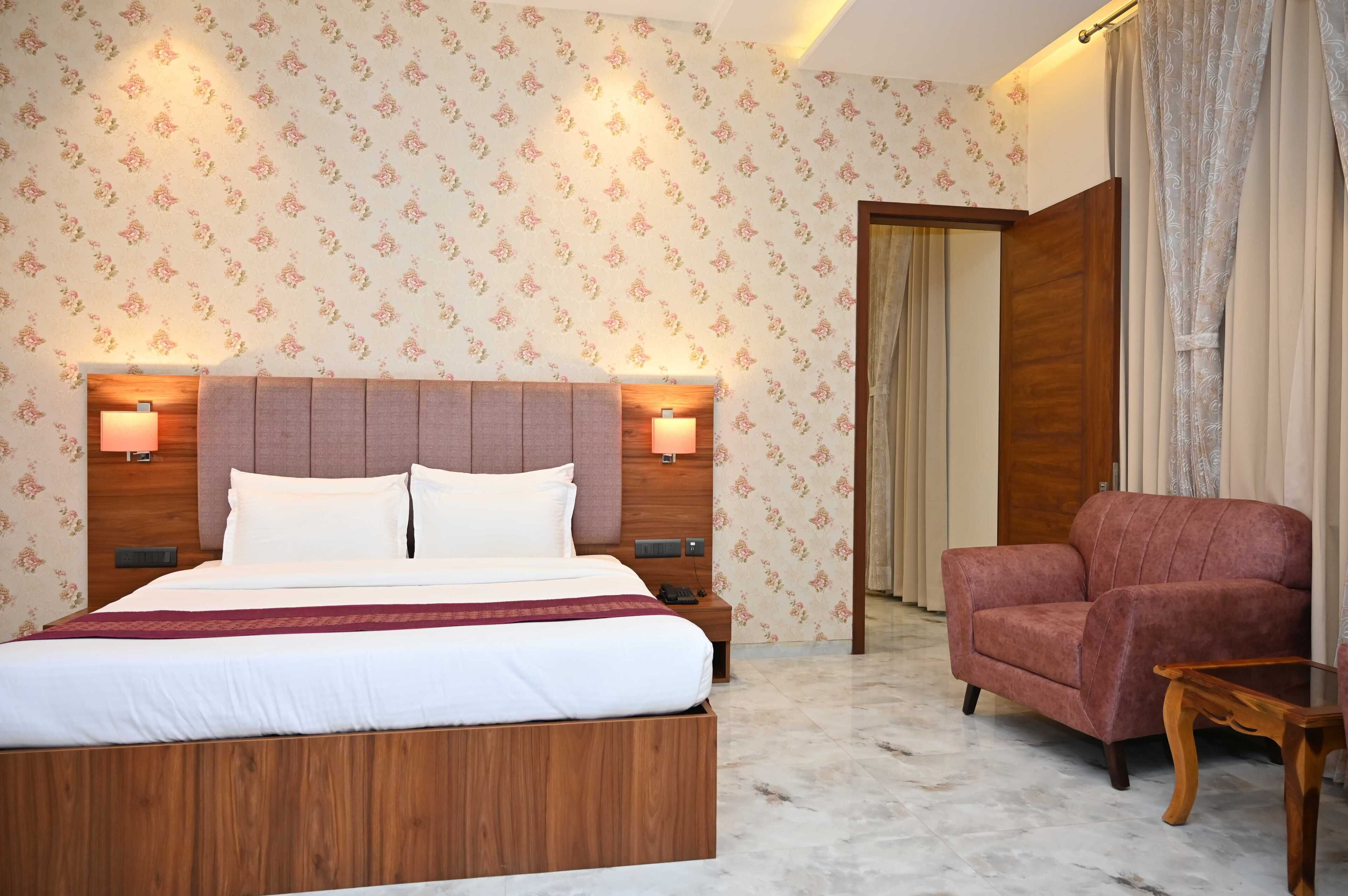 A hotel room with a large bed, a wooden headboard, two bedside lamps, a red armchair, a wooden nightstand, and a wooden table.