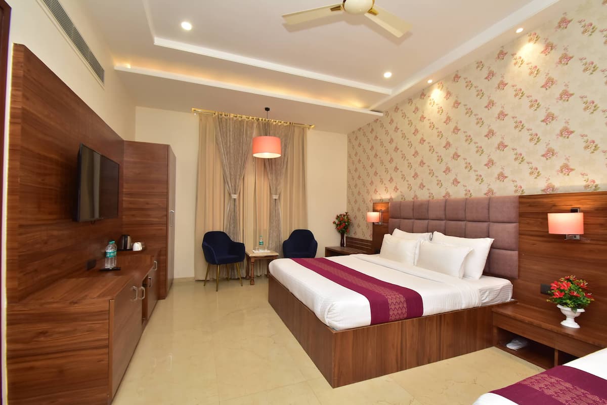 Une chambre d’hôtel avec un lit en bois, une télévision, un bureau avec des chaises et un ventilateur de plafond.