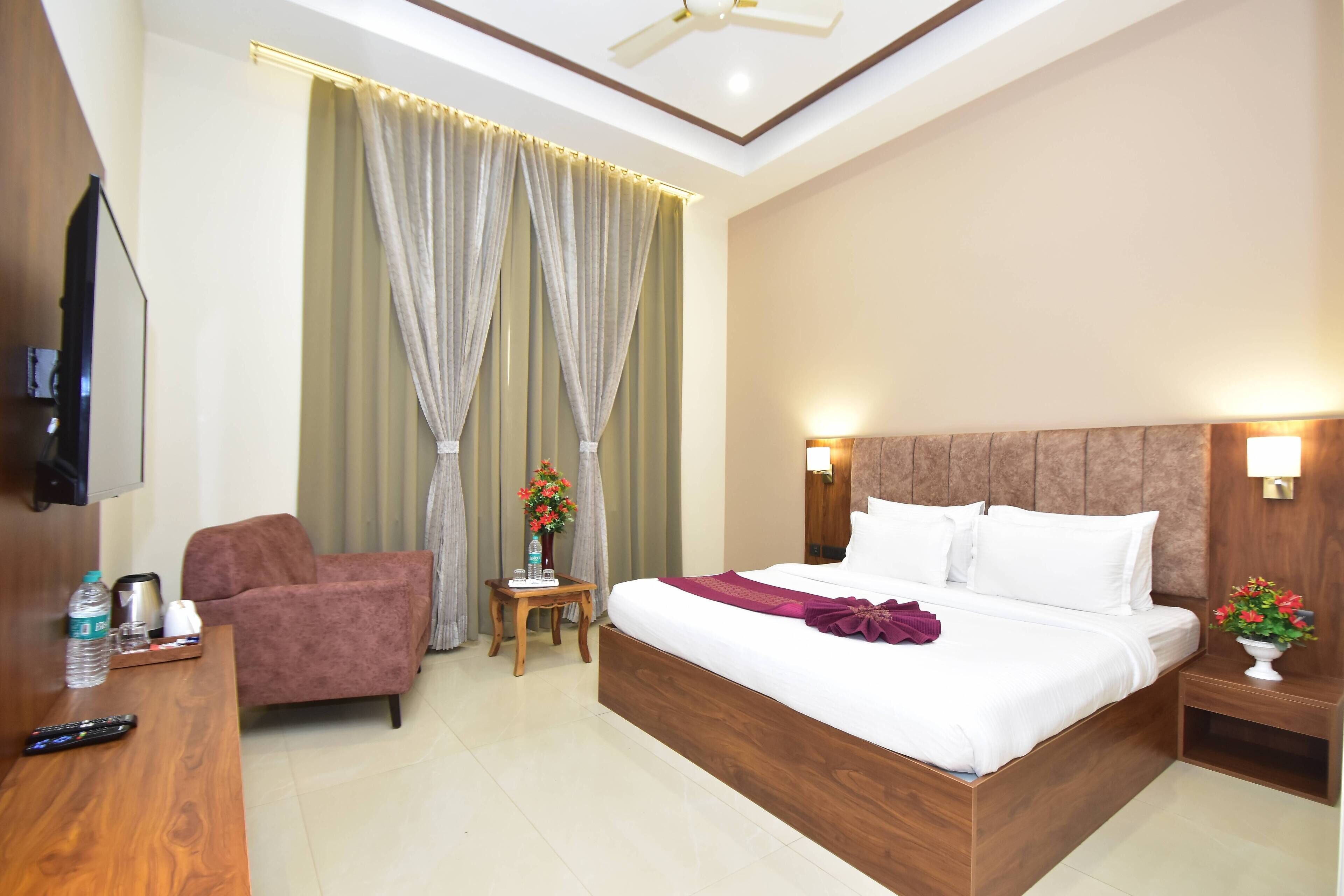 Habitación de hotel con una cama grande, un cabecero de madera, un televisor montado en la pared, una mesita con un jarrón de flores y una silla.