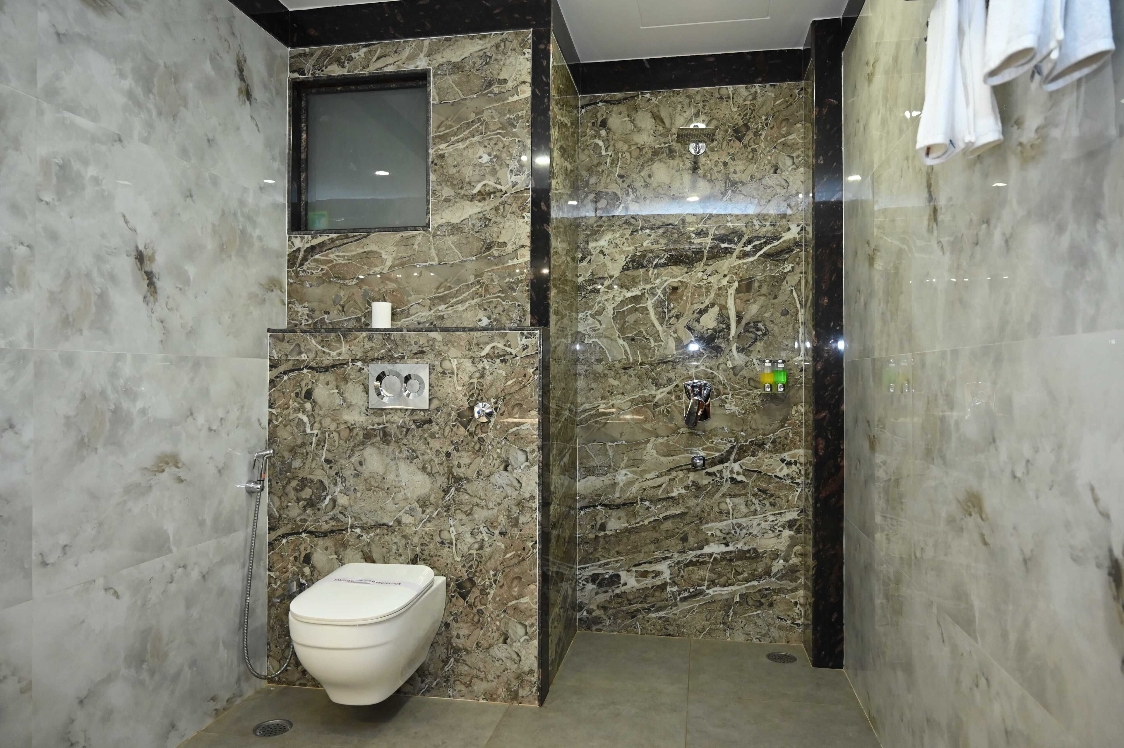 A modern bathroom with a marble wall, a toilet, a shower area, and a towel rack.