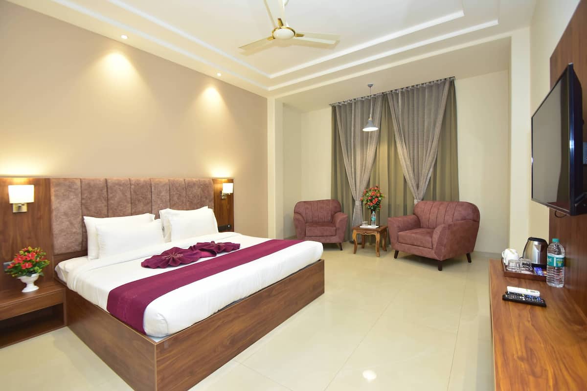 Une chambre d’hôtel avec un grand lit, deux fauteuils, une télévision et une table basse.