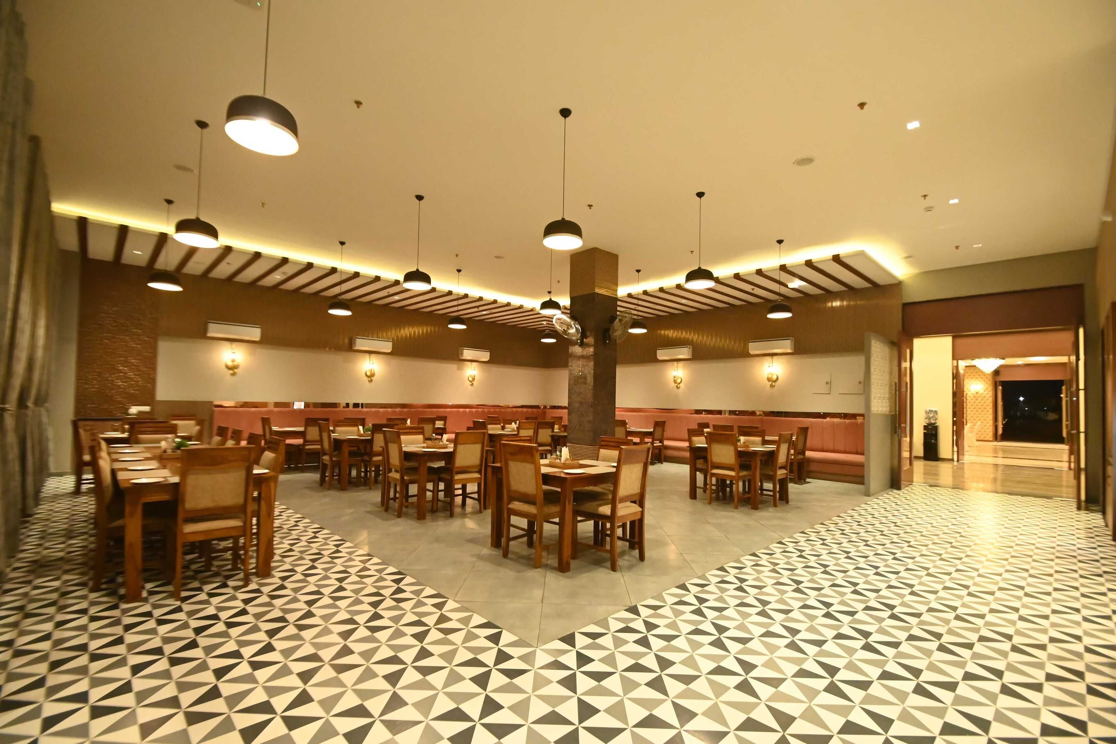 Un comedor amplio con varias mesas y sillas, suelo estampado e iluminación colgante.