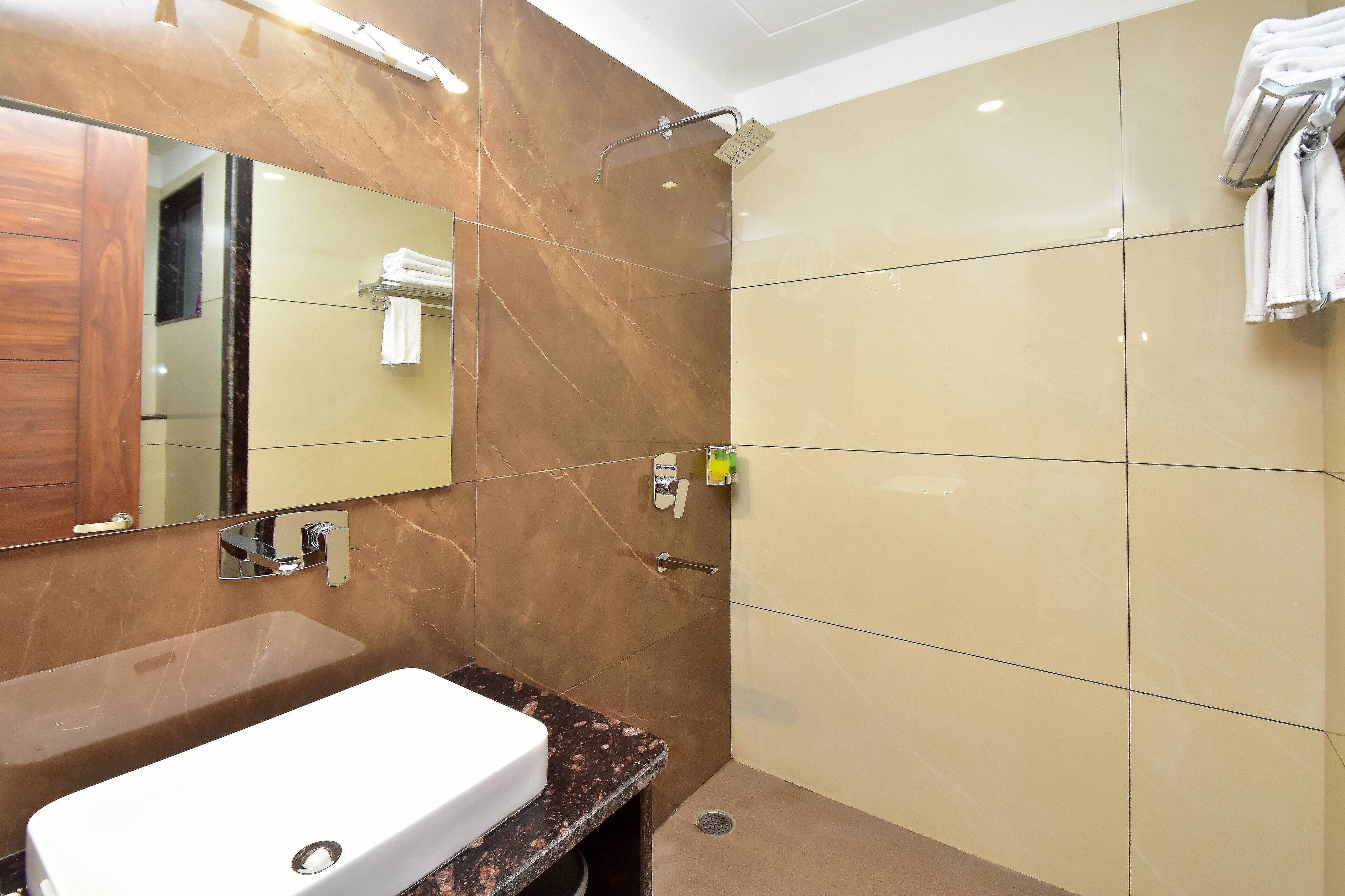 Een badkamer met een witte wastafel, een spiegel, een douche met handdouche en een handdoekrek.
