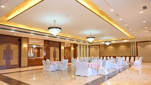 A banquet hall with white chairs and tables, chandeliers, and a polished floor. - Hotel ShyamLeela - Khatushyamji (Shri Madhopur)