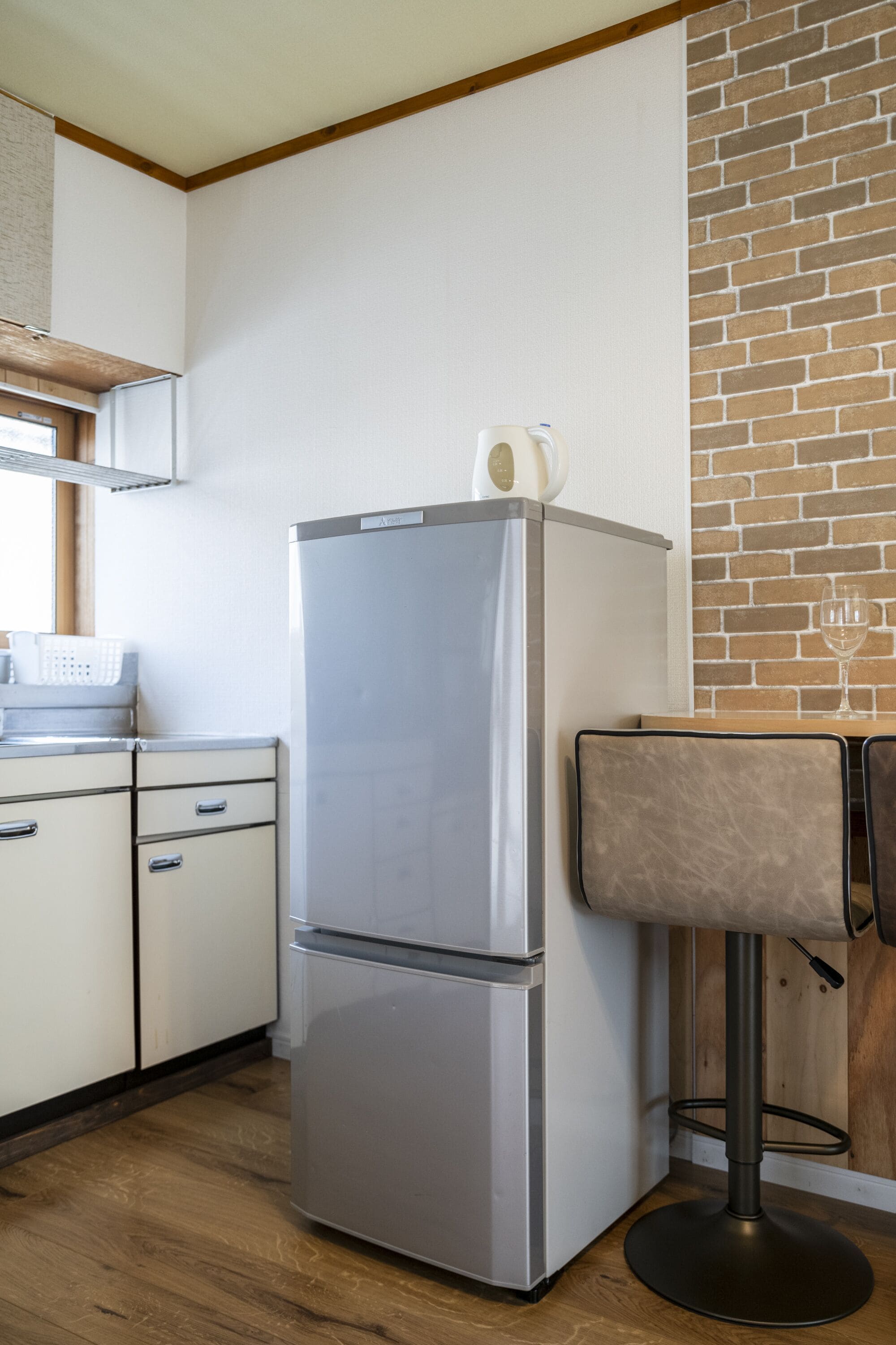 A kitchen with a stainless steel refrigerator, wooden cabinets, a brick accent wall, and a bar stool.