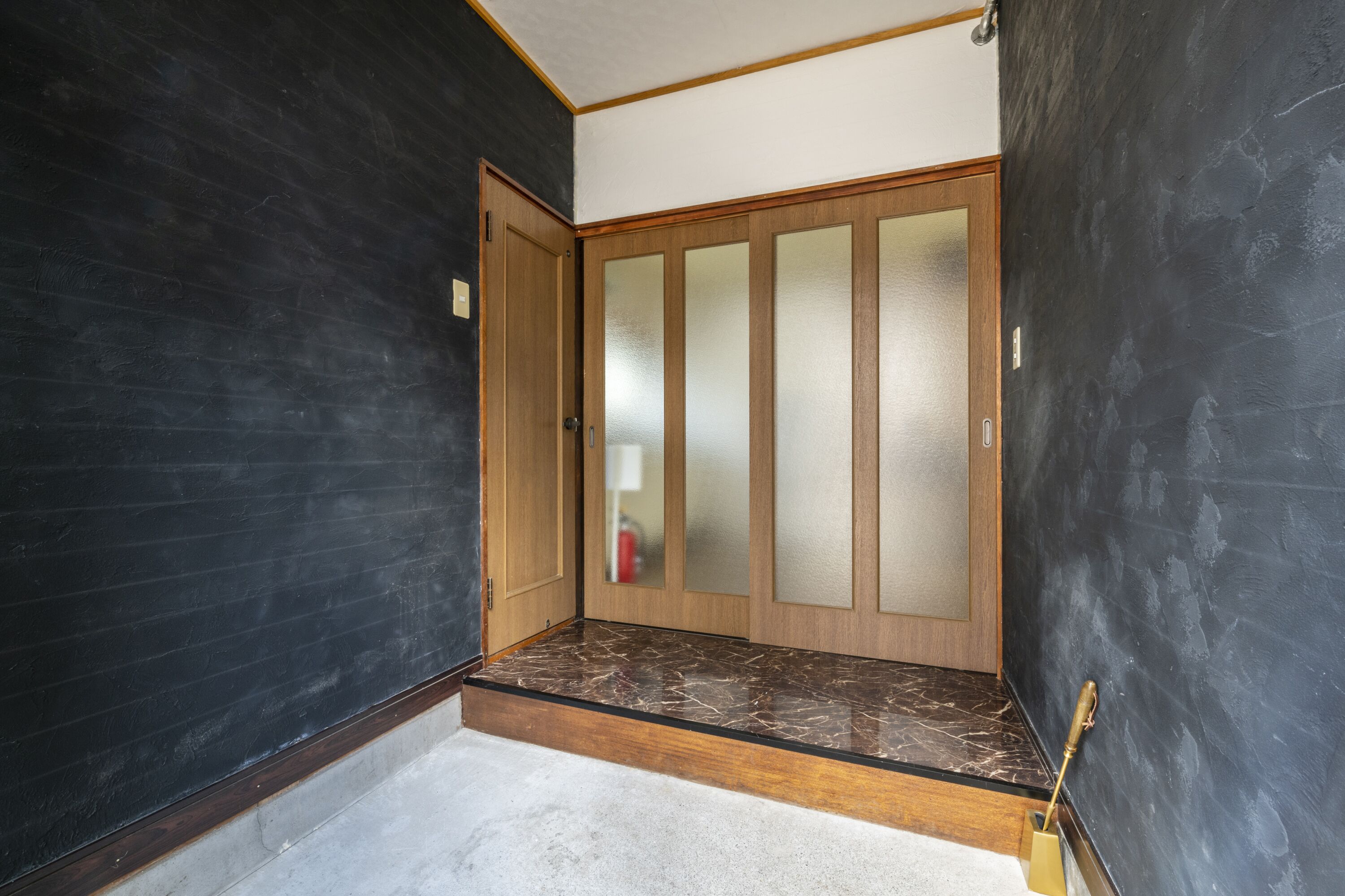 A room with dark walls, a wooden door with frosted glass panels, and a marble-topped bench.