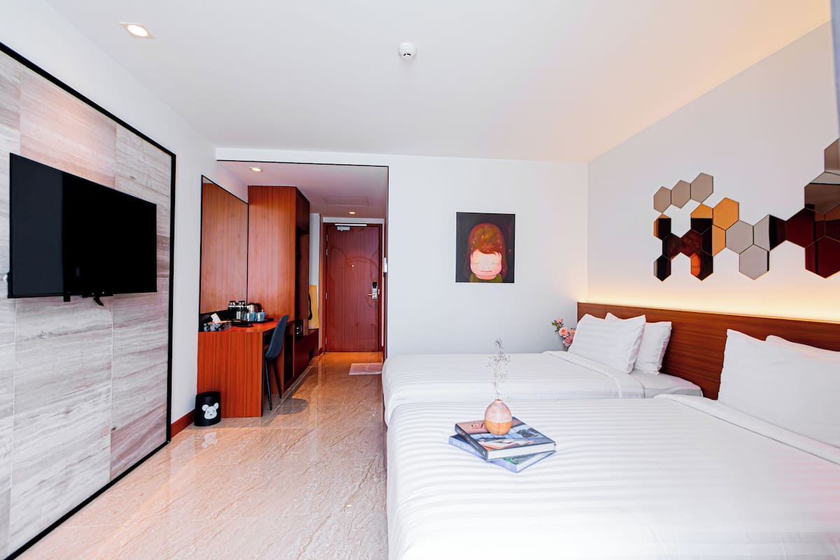 A modern hotel room with a large bed, a flat-screen TV mounted on the wall, a wooden desk, and a small kitchenette.