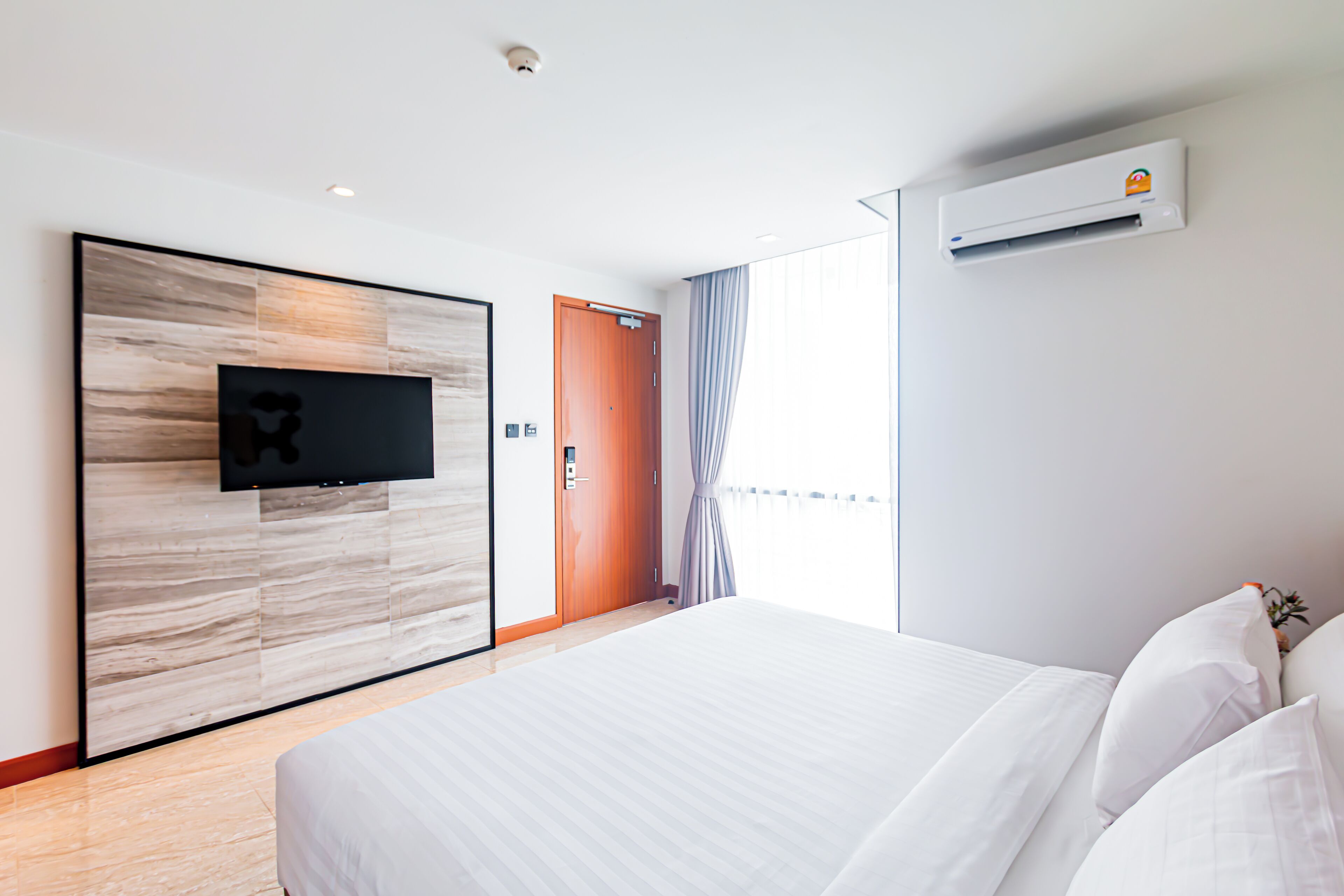 Une chambre d’hôtel dotée d’un grand lit, d’un téléviseur à écran plat fixé sur un mur en panneaux de bois, d’un système de climatisation et offrant une vue sur l’extérieur.