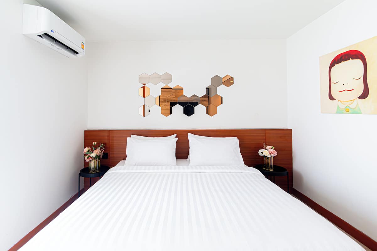A hotel room with a large bed, two nightstands, a wall-mounted air conditioner, and a geometric wall art piece.