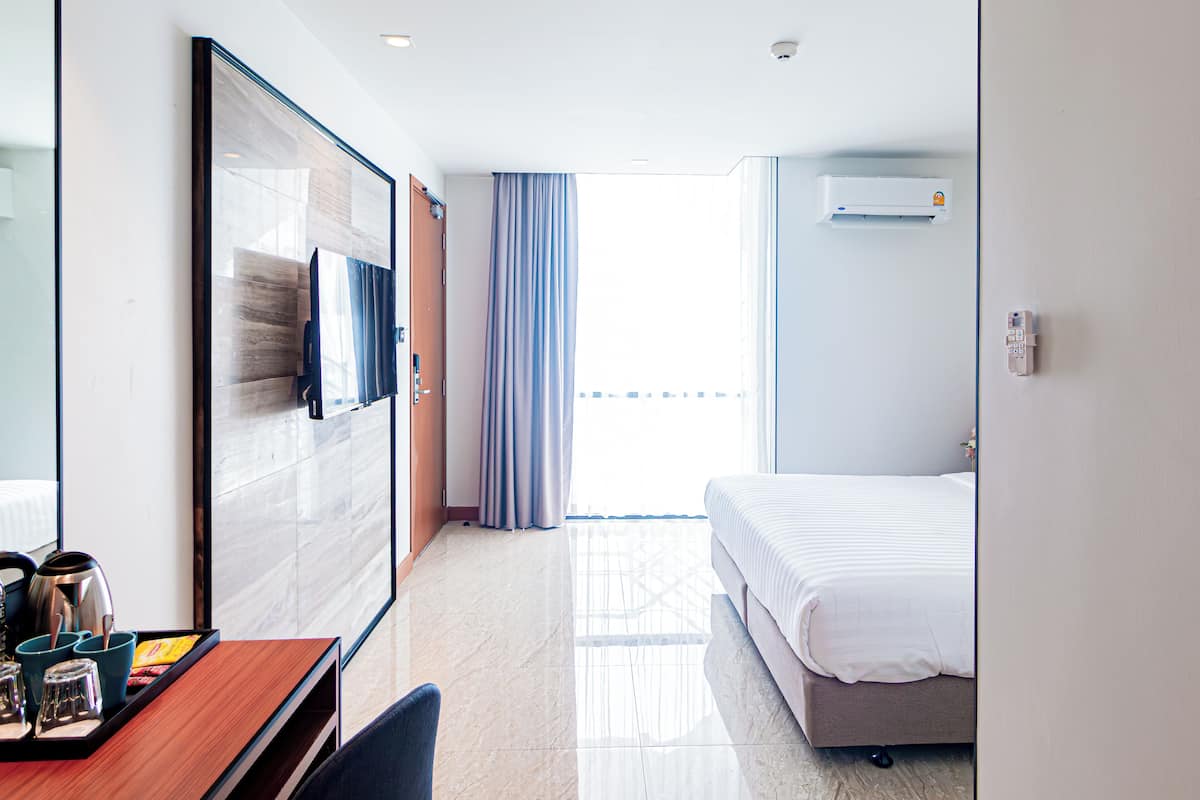 A hotel room with a bed, a desk with a chair, a TV, and a window with curtains.