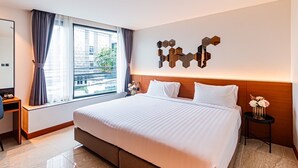 A hotel room with a large bed, a desk, a chair, a window with curtains, and a wall-mounted mirror. - Frame Hotel Bangkok (Bangkok)