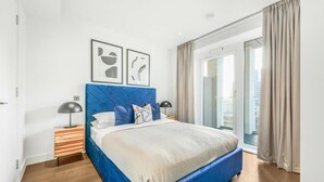 Un dormitorio moderno con cabecera azul, una cama grande, dos mesitas de noche y vistas a un balcón.