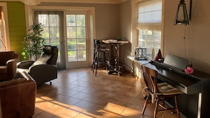 A living room with a piano, a dining table, and a large window.
