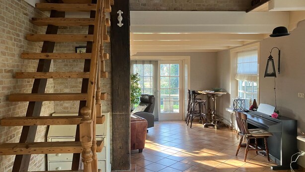 A spacious room with a wooden staircase, a piano, and a comfortable seating area.