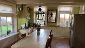 A kitchen with a dining table, chairs, a refrigerator, and a window with a view of the outdoors.