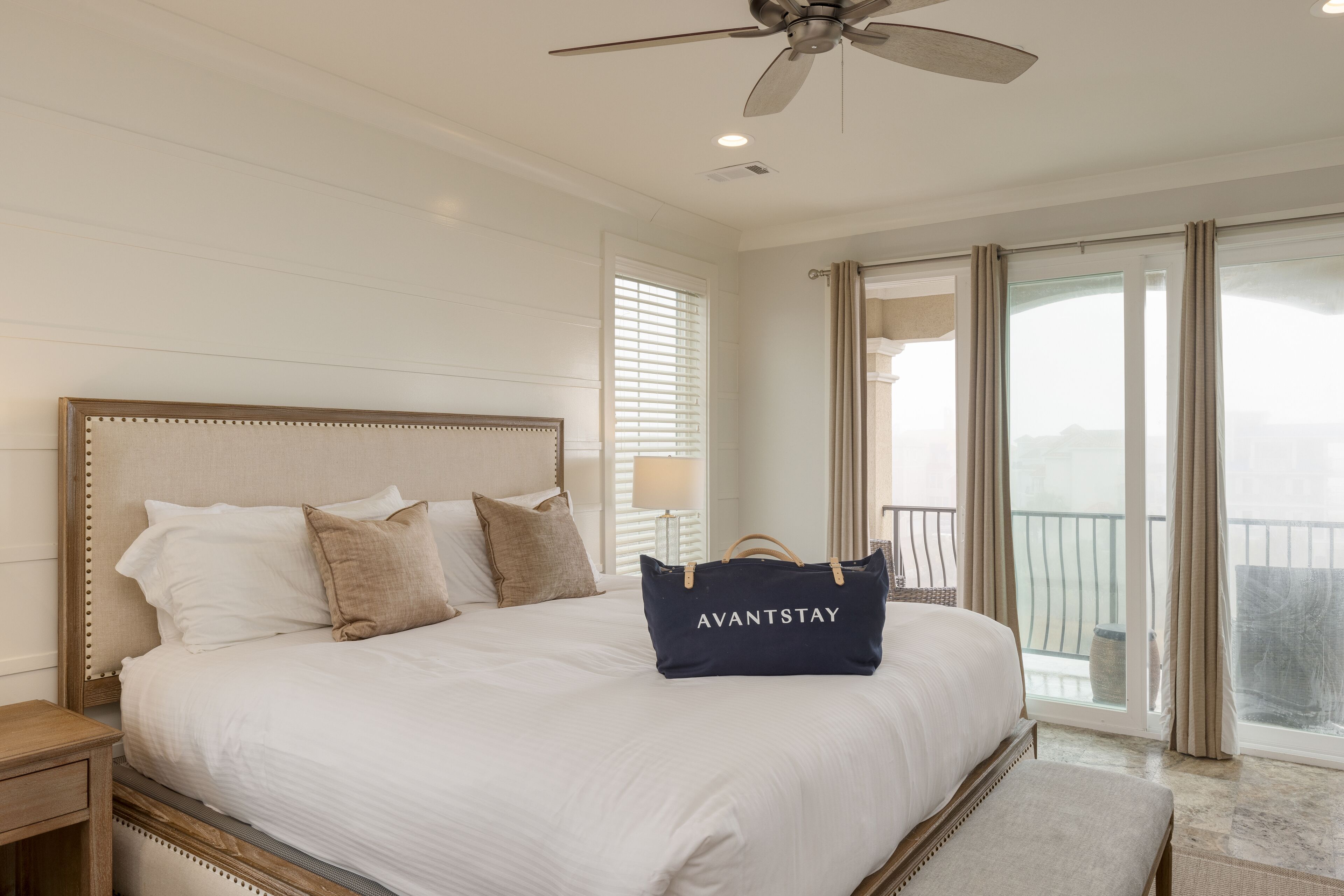 Habitación de hotel con una cama grande, un ventilador de techo y vistas al exterior a través de amplias ventanas.