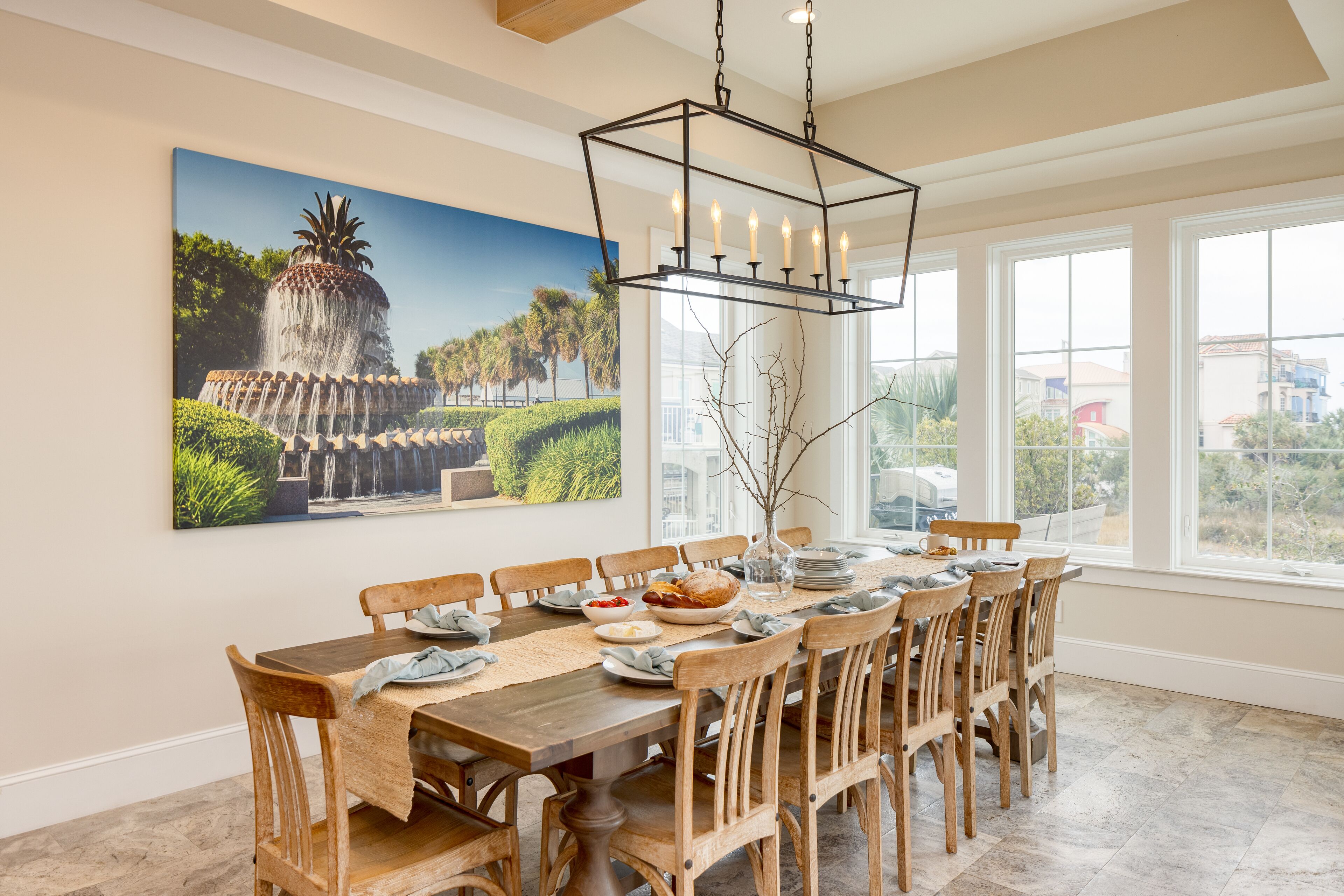A dining area with a large table, wooden chairs, a chandelier, and a large painting of a fountain.
