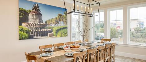 A dining area with a large table, wooden chairs, a chandelier, and a large painting of a fountain.
