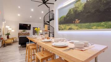 A modern dining area with a wooden table set for four, a black spiral staircase, and a large window with a nature scene.