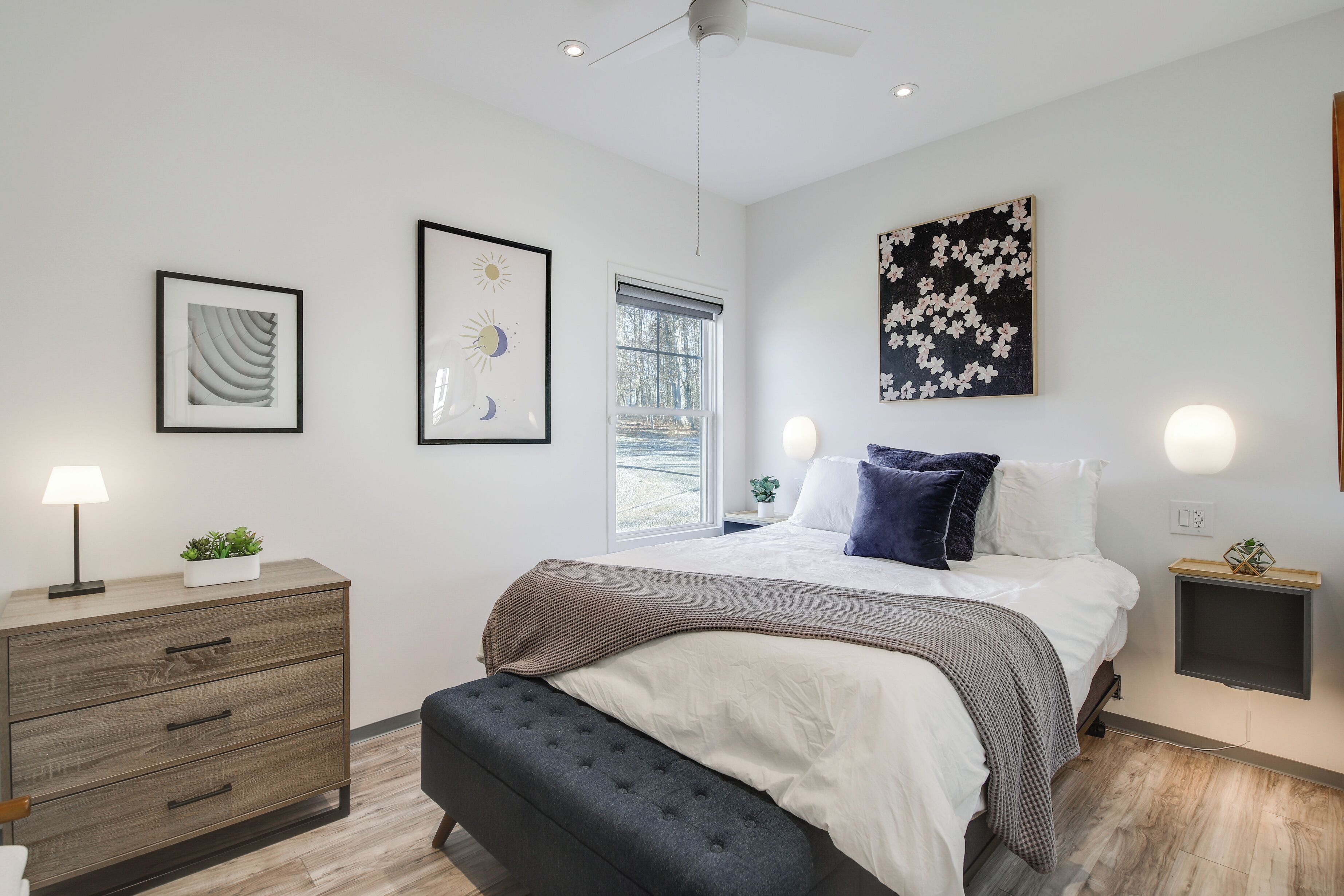 Une chambre à coucher moderne, avec un lit, des tables de chevet, une commode et des œuvres d’art accrochées aux murs.