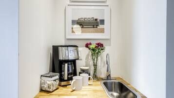 A kitchenette with a coffee maker, two mugs, a sink, and a vase with flowers.