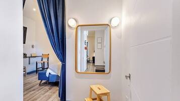 Una habitación de hotel con una cama, un taburete de madera, un espejo y una cortina.