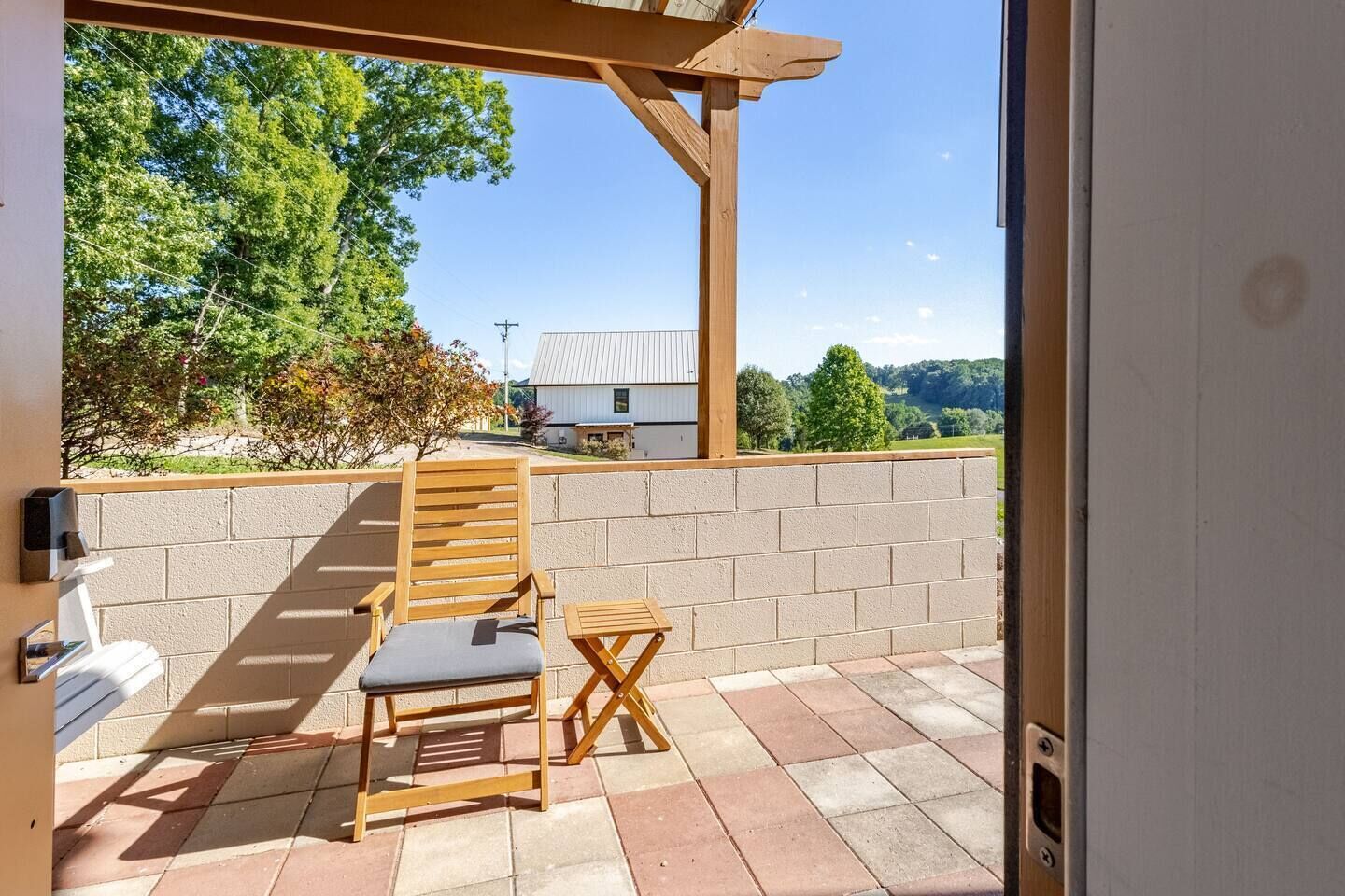 Een terras met een houten stoel en tafel, een bakstenen muur en uitzicht op een huis en bomen.