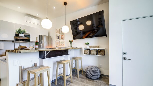 Una cocina moderna con barra, taburetes de madera, un televisor grande y un refrigerador blanco.
