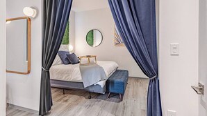 A bedroom with a bed, bedside table, bench, and a mirror on the wall.