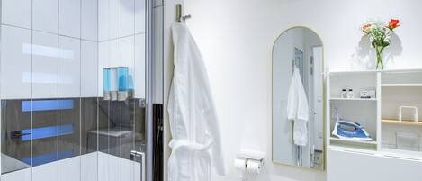 A modern bathroom with a glass shower enclosure, a white robe hanging on a rack, a mirror with a gold frame, and a shelf with toiletries.